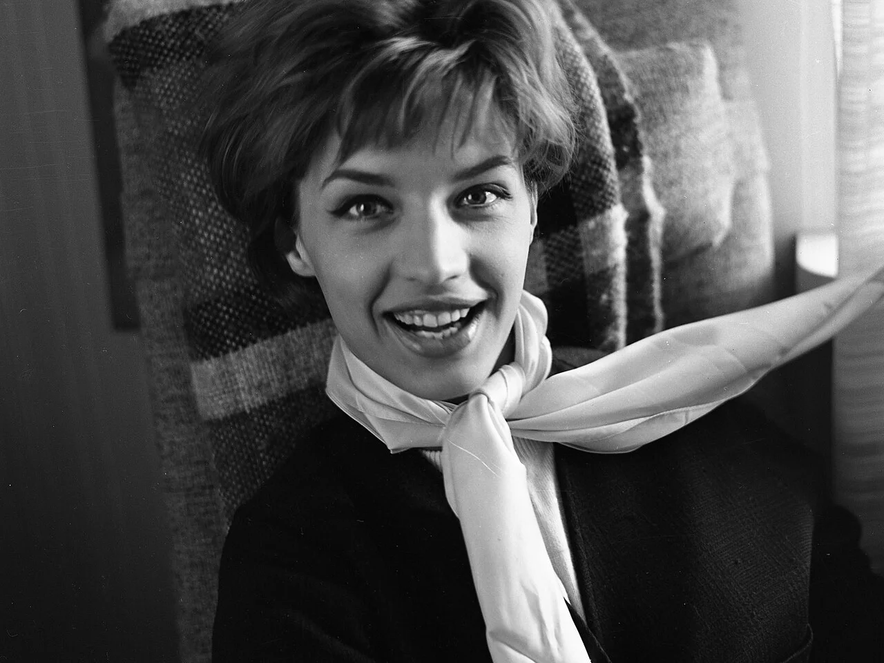 Svartvitt porträtt av en leende Lill-Babs med kort hår och ljus sidenscarf, fotograferad 1961